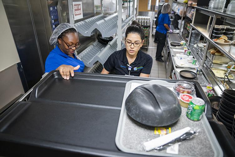 Dining Service Associate Symone Buckles, from left, and Nutritional Services Supervisor Jessica Contreras load trays of lunches for patients