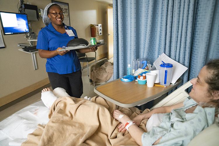 Dining Service Associate Symone Buckles delivers lunch and a smile to a T11 patient