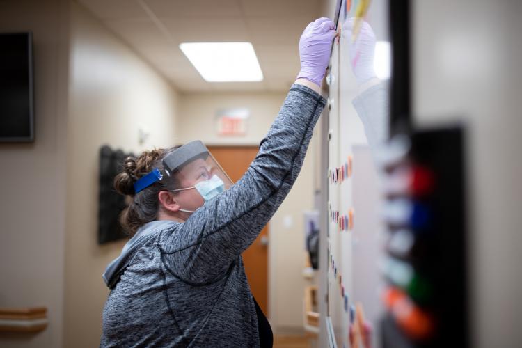 Dr. Katherine Buck, Director of Behavioral Medicine at JPS Health Network in Fort Worth, Texas, moves a magnet on a whiteboard to show she has taken her turn to see a patient in the Post COVID Recovery Clinic. 