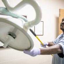 Derrick Christor dusts a lamp in an Emergency Department examination room.