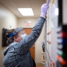 Dr. Katherine Buck, Director of Behavioral Medicine at JPS Health Network in Fort Worth, Texas, moves a magnet on a whiteboard to show she has taken her turn to see a patient in the Post COVID Recovery Clinic. 